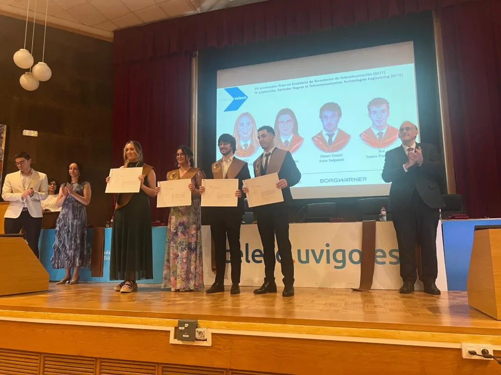 Catro graduados amosan o seu diploma mentres o público aplaude na graduación de Vigo