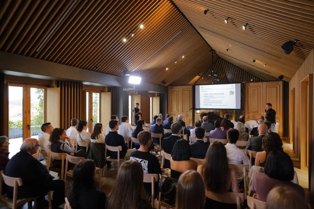 Sala con ventás e teito de listóns de madeira onde numeroso público segue un relatorio