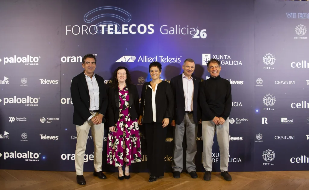 Tres homes e dúas mulleres posan diante do panel do foro, cuberto de logotipos de patrocinadores