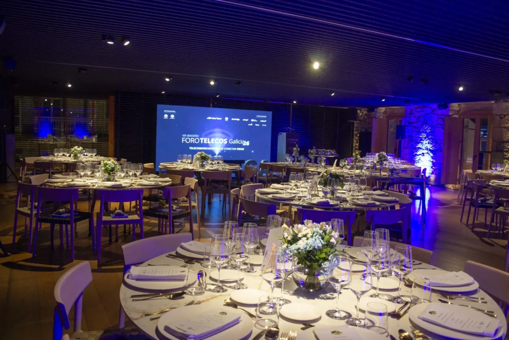 O salón, con mesas redondas postas e flores, preparado para a cea de gala