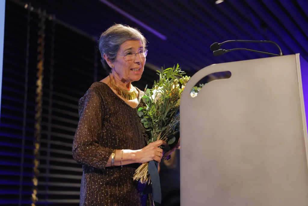 Unha muller maior con lentes sostén un ramo de flores e fala desde un atril
